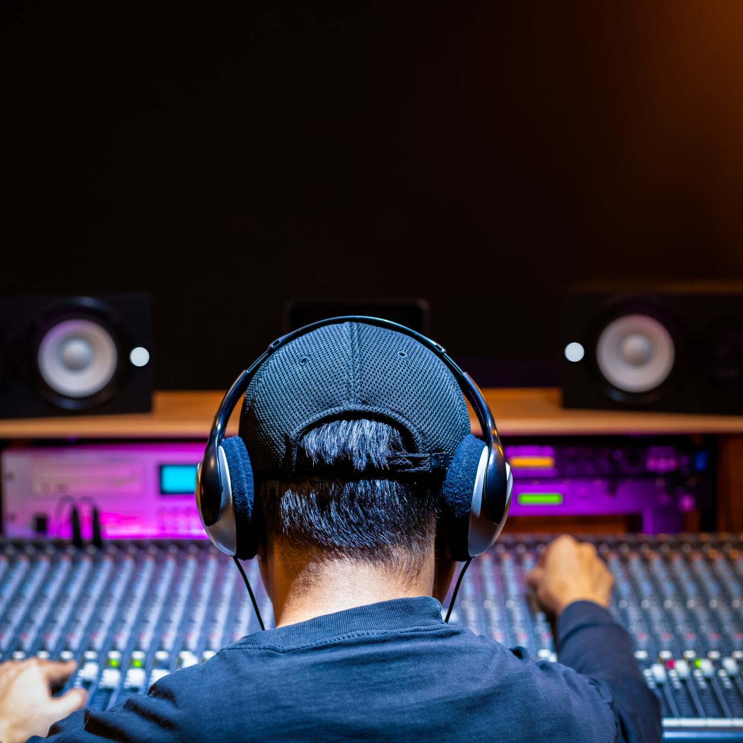 A man in a music studio wearing headphones while adjusting a mixing desk.