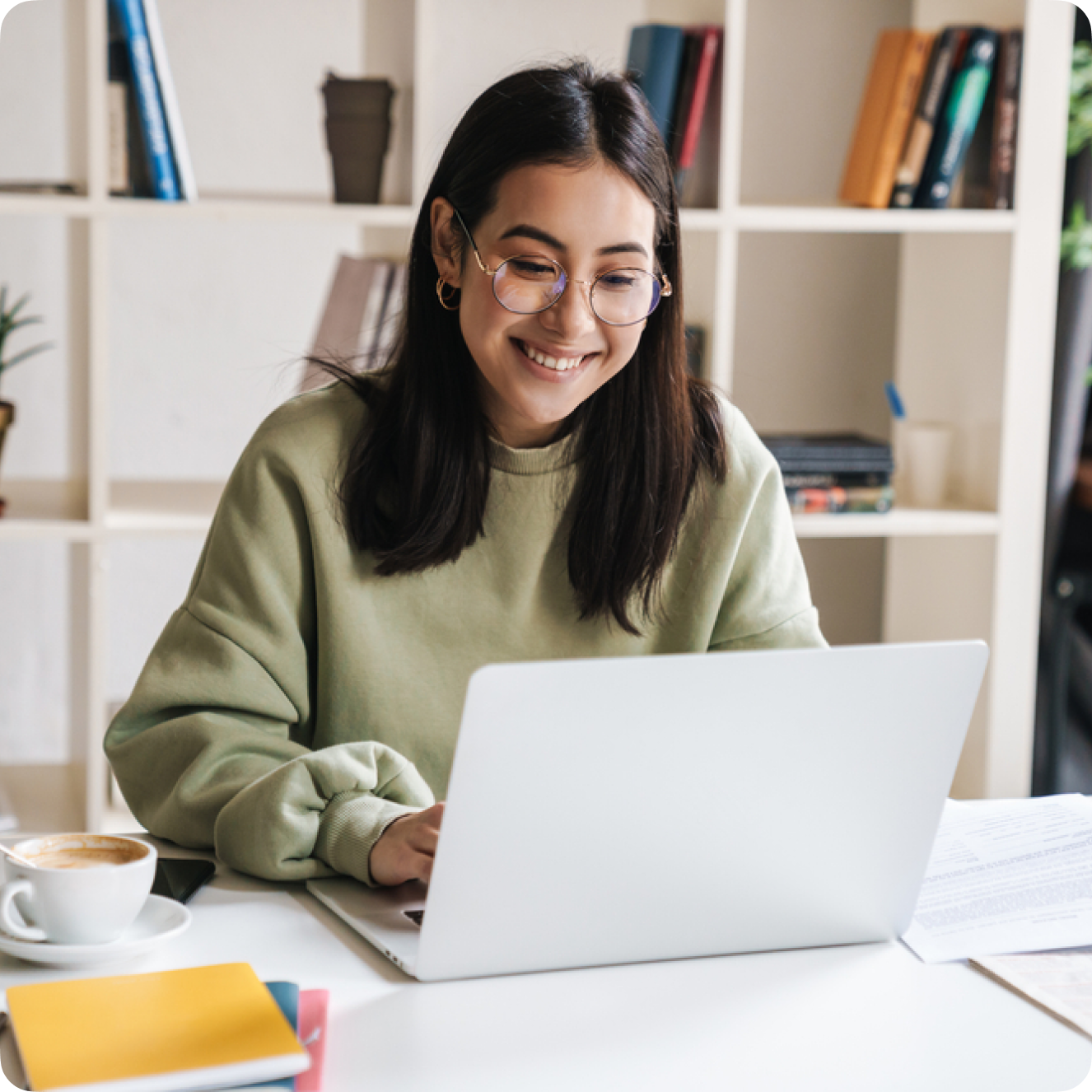 Female-presenting marketing professional wearing a sage green sweater using a laptop and smiling.