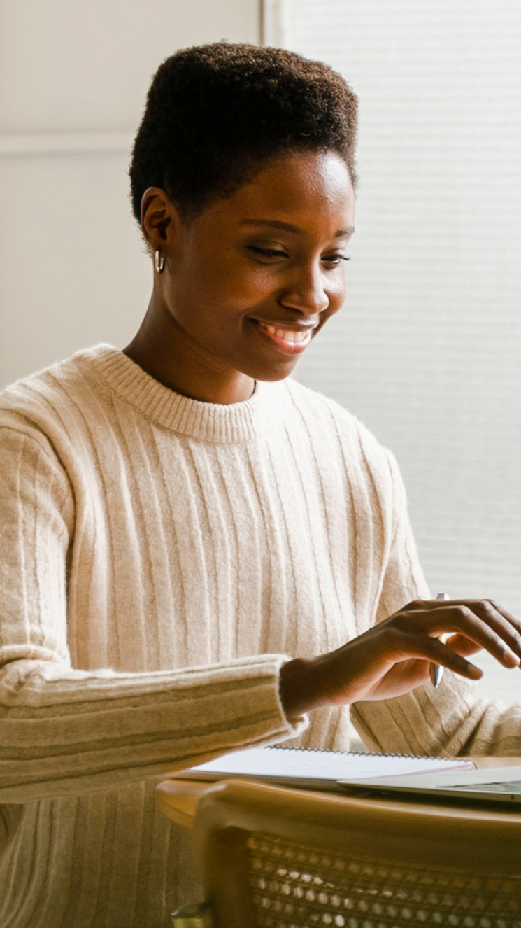 A female-presenting person in a modern room, working on a laptop.